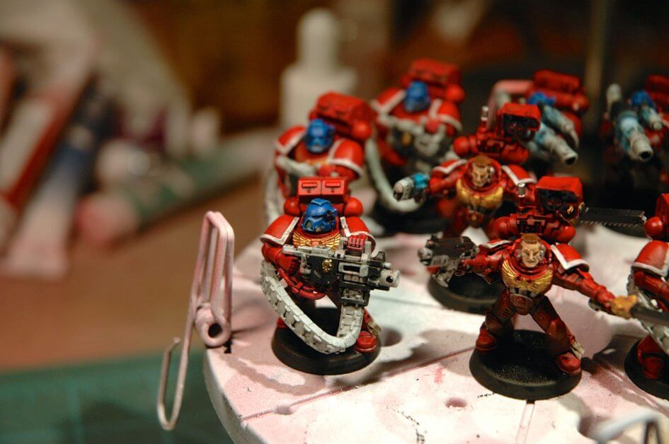Blood angel space marines for warhammer 40k - wip - A close-up of red armored miniature soldiers being painted, with focused detailing on the headgear and weaponry.