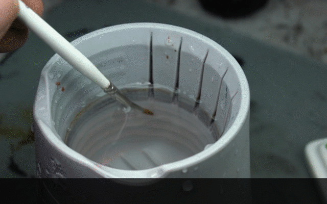 Hand cleaning a paintbrush against the textured ridges inside the Citadel water pot