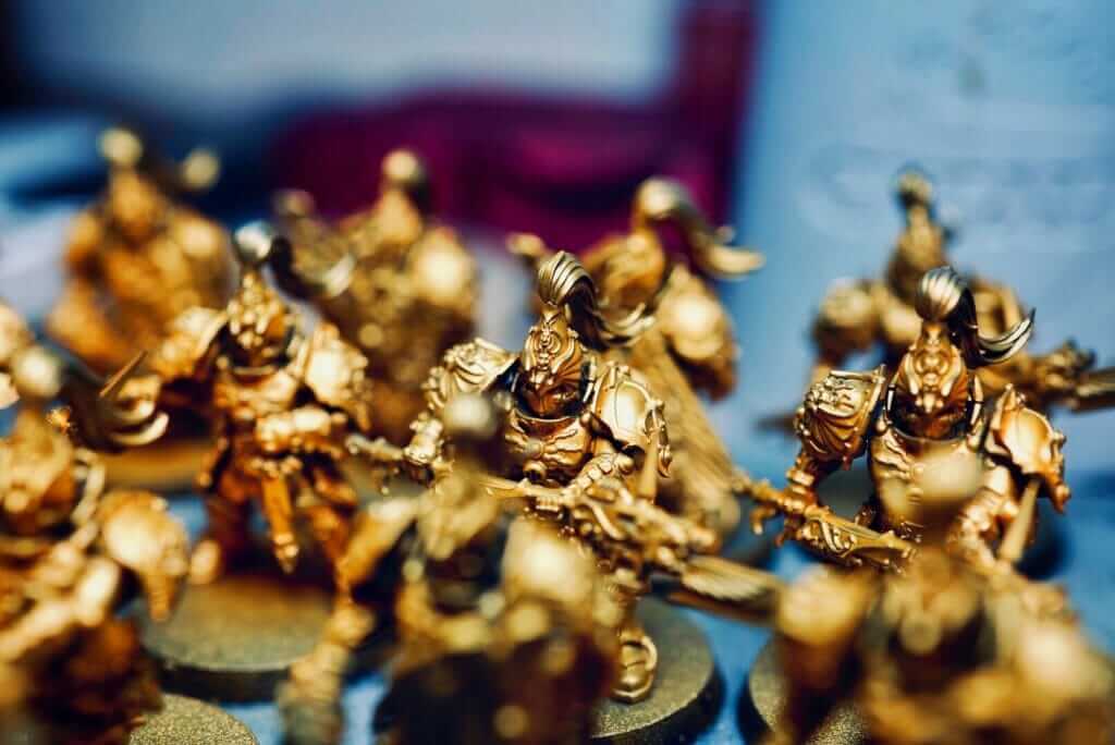 Macro shot of golden-painted miniature figures, highlighting the intricate details achievable through skilled painting