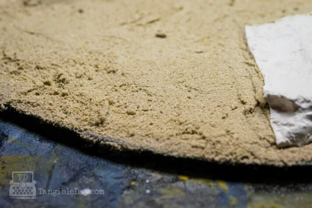 Premixed sanded tile grout applied to a round miniature base to create a dirt and mud ground texture before painting.