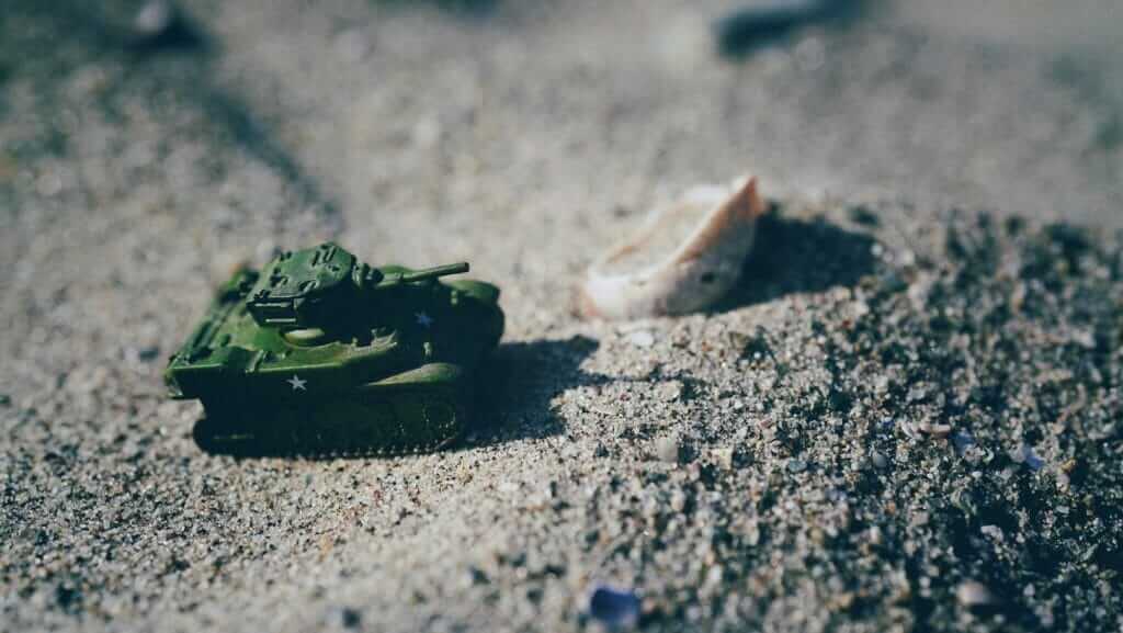 Small green military tank model on sandy terrain with a seashell in the background