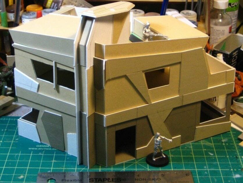 Large scratch-built sci-fi building made from foamboard with sprue strips used as structural edging, shown on a hobby cutting mat to demonstrate reinforcing terrain surfaces.