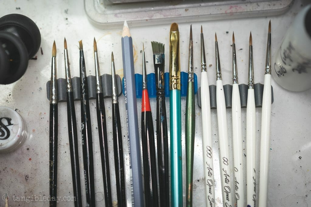 Assorted miniature-painting brushes resting in a desktop brush holder, illustrating how sprues can be repurposed into simple drying racks for hobby tools