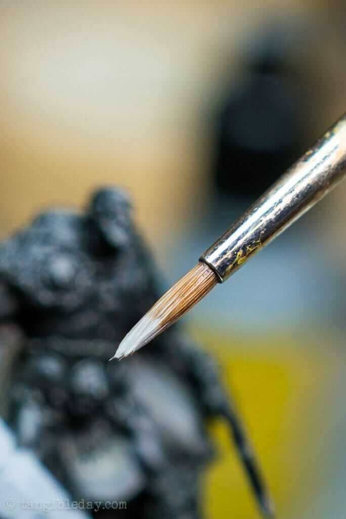 Miniature Paint Brush Care Tutorial - how to care for brushes for miniature painting - Close up photo of gray paint loaded on the tip of a miniature paint brush