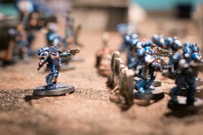 The History of Tabletop Wargaming - Miniature wargaming history through the ages, milestones and key points - metallic blue painted space marine points his gun at the enemy on a tabletop wargaming space
