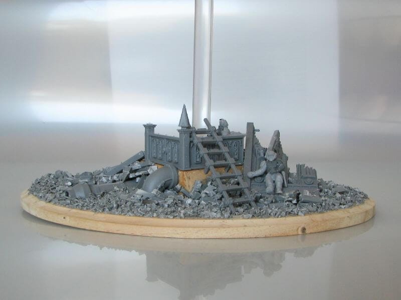 Circular diorama base covered in chopped sprue rubble with a central ruined structure, pipes, and debris, showing how recycled sprues can create detailed terrain for miniature hobby projects