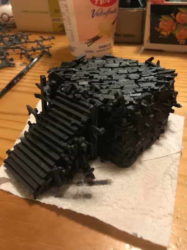 Chunky black terrain block built from tightly stacked plastic sprue pieces with a sprue staircase, shown on a hobby desk as an example of recycled sprue terrain for miniature wargaming