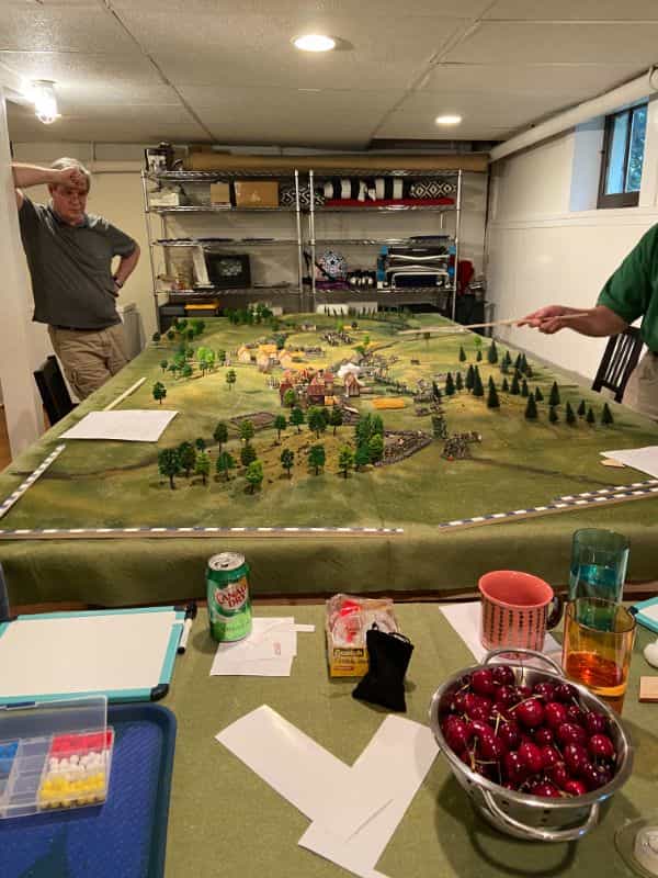 AI Enhanced Wargaming and Tabletop RPGs (Tips and Uses) - Carnage and Glory II played with food and drink nearby. Two gamers hold rulers and inspect a rulebook