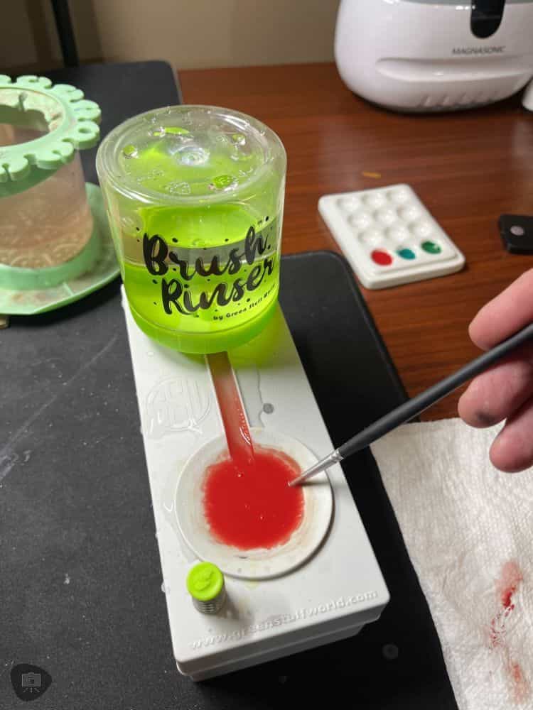 Green Stuff World Brush Rinser (Review) - best gadget to keep clean water available for miniature painters - user cleaning off their brush in the rinser with red paint in the water