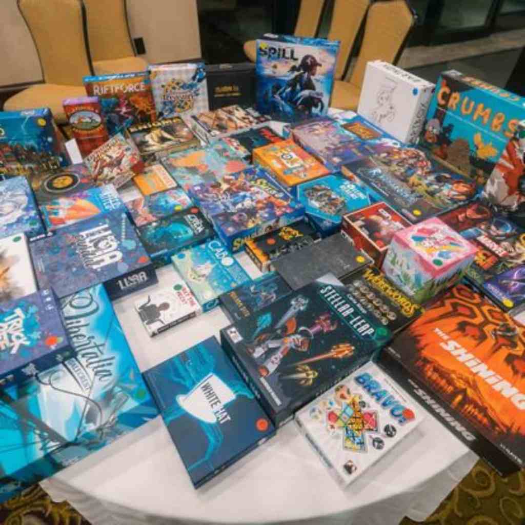 Running a Successful Hobby Gaming Convention: The Hidden Magic and Mayhem Behind CaptainCon - Pile of Board games on a table for charity drawing