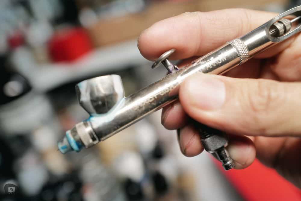 Hand holding an airbrush, showcasing the tool's detailed craftsmanship and potential for precision in miniature painting