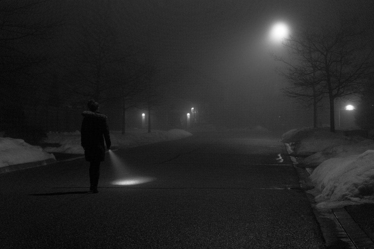 person in black jacket walking on dark road - blackout