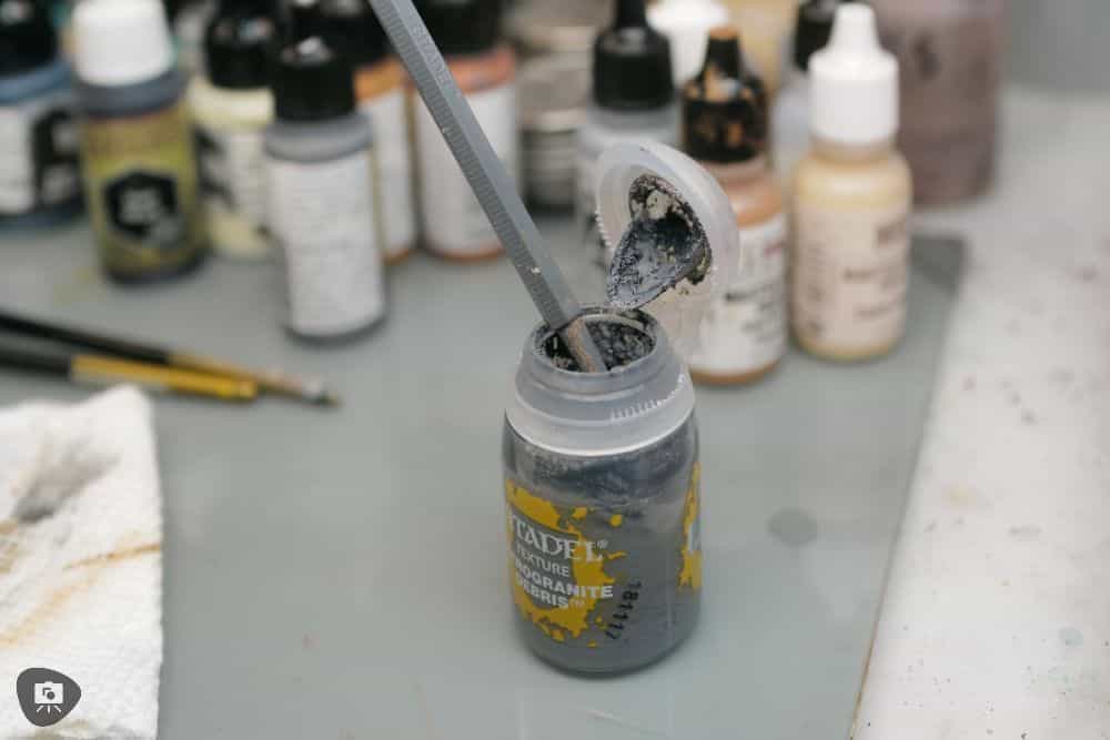 My Favorite Citadel Technical Paint and How to Use Astrogranite Debris (Review) - citadel texture paint astrogranite review and tutorial - A Citadel Texture Tool sticking out of a pot of Astrogranite Debris paint