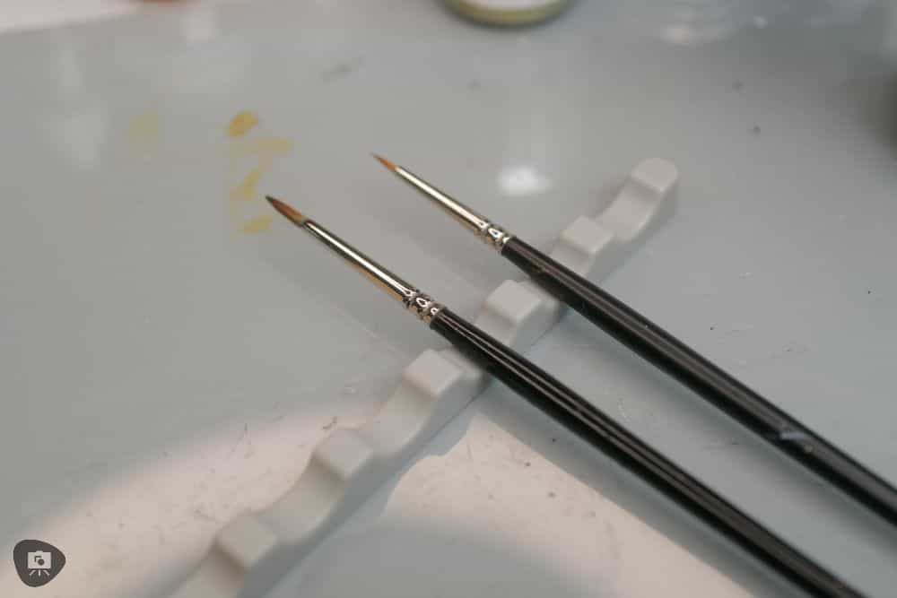 Miniature Paint Brush Care Tutorial - how to care for brushes for miniature painting - two brushes laying horizontally on a hobby desk
