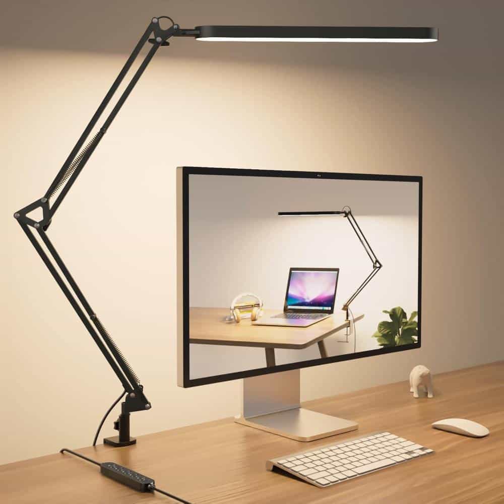 SKYLEO LED swing-arm desk lamp clamped to a wooden workspace, positioned above a computer monitor with an adjustable metal arm and slim overhead light bar.