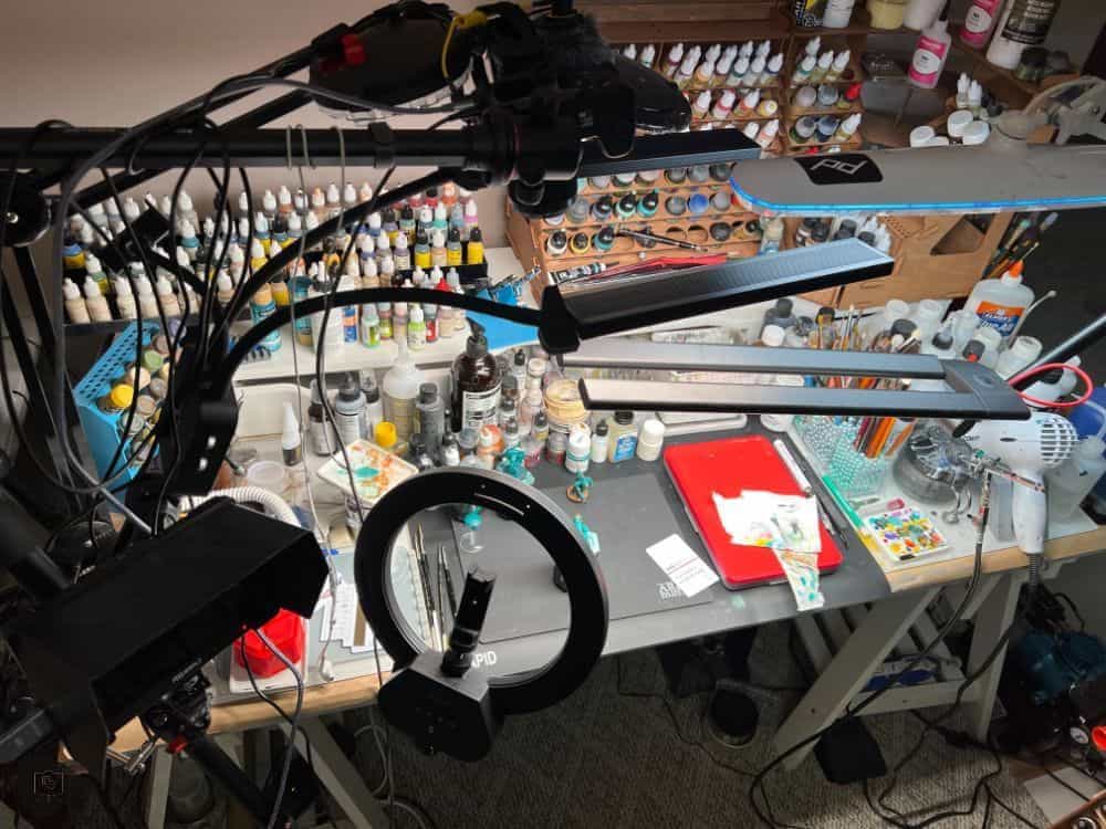 Overhead shot of a well-lit miniature painting workspace with multiple task lamps and hobby tools.