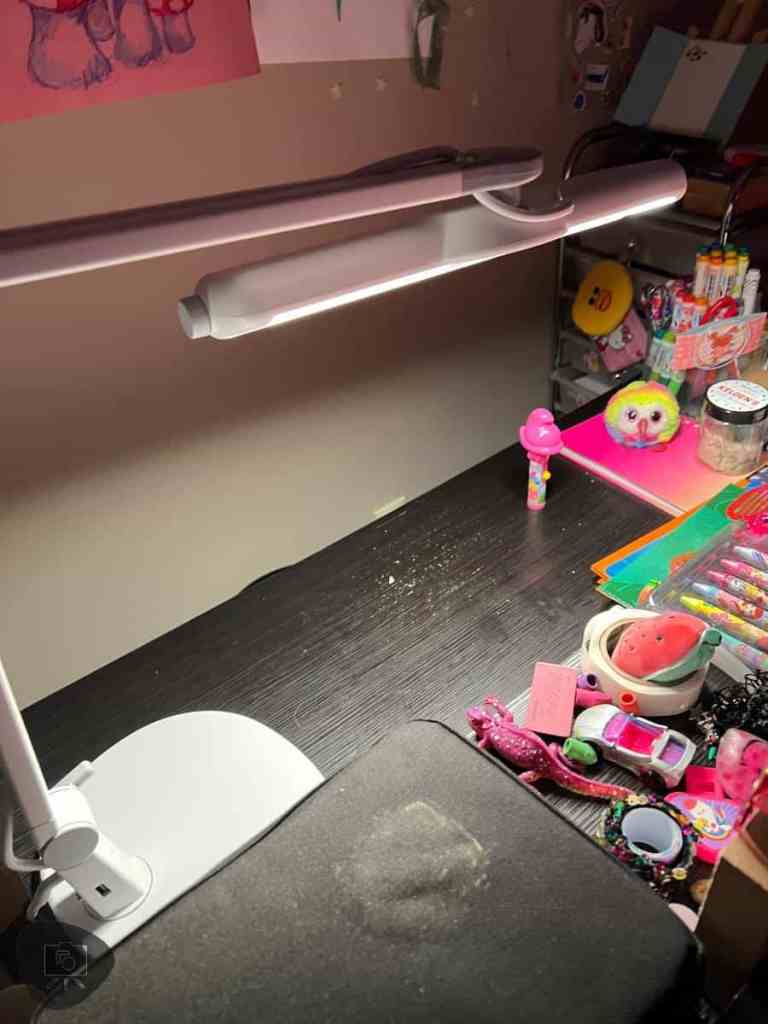 The BenQ MindDuo 2 lamp casts a bright, focused light over a child's desk area, revealing a variety of playful stationery and craft materials