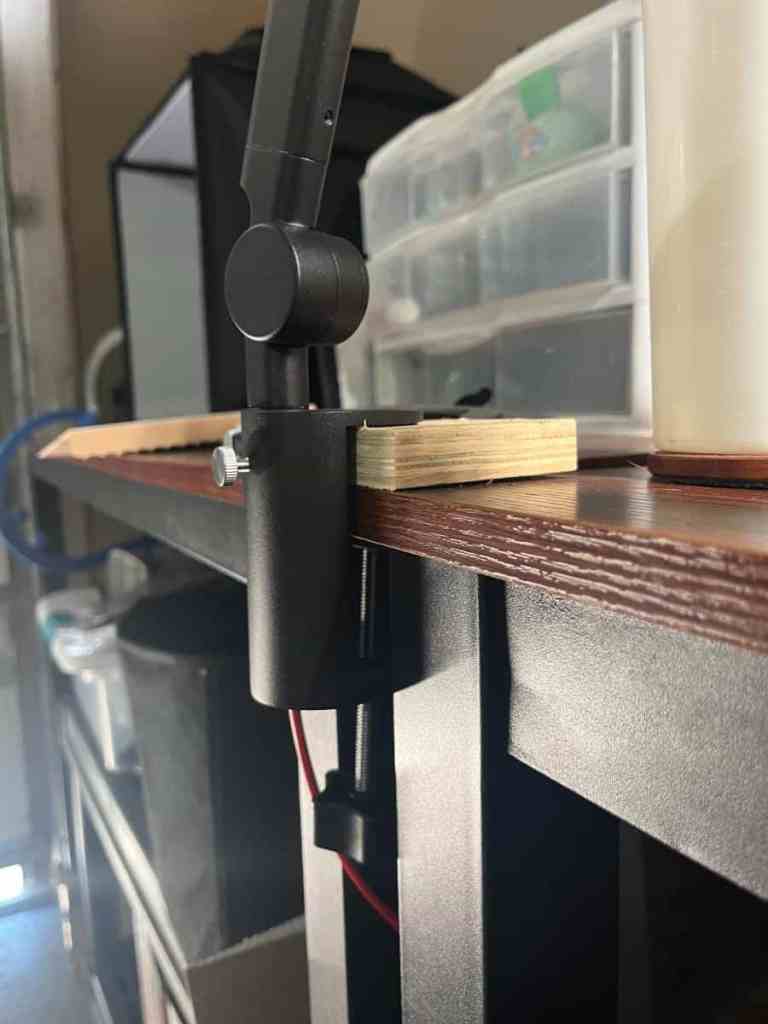 Close-up of a black desk lamp clamp attached to a wooden table edge with a light switch and cable visible