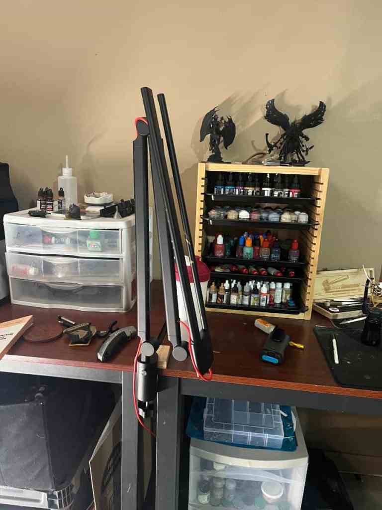 A workspace showing the Redgrass R9 desk lamp extending over a desk cluttered with painting supplies and miniatures