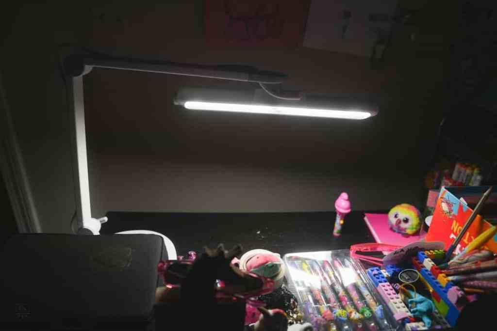 A dimly lit room featuring the BenQ MindDuo 2 desk lamp illuminating a child's creative workspace strewn with colorful art supplies