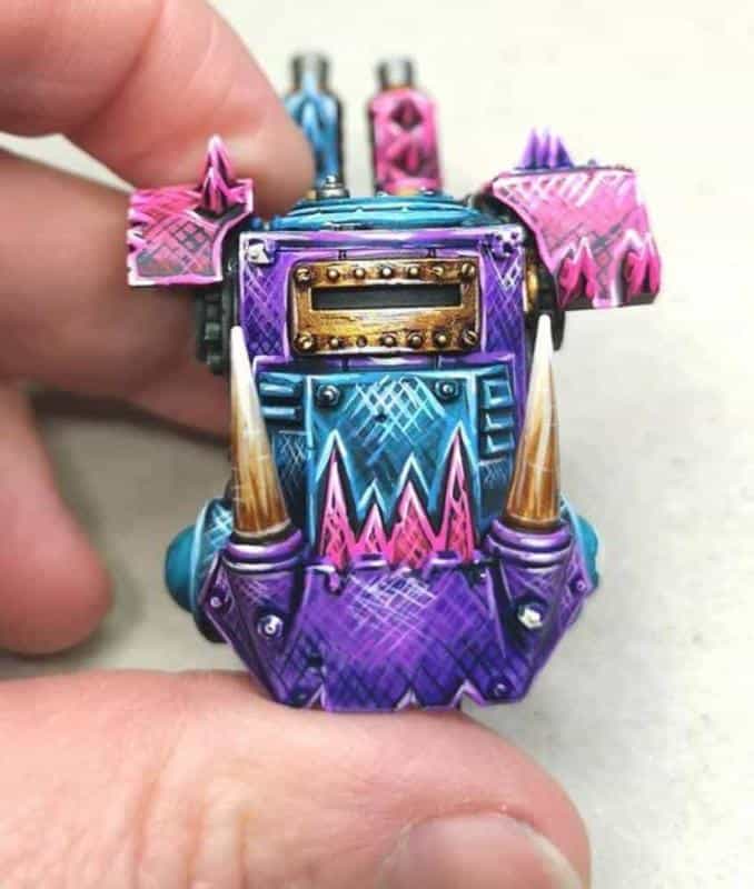 Hand holding a brightly painted Ork armor plate featuring purple, blue, and pink gradients with jagged patterns and metallic details.