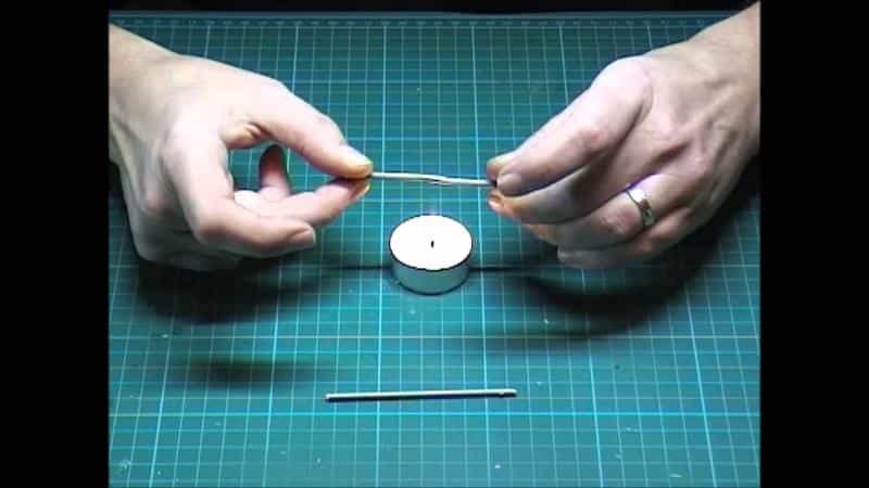 Close-up of stretched sprue being heated and pulled into thin antenna-like cables, used to demonstrate how modelers create fine detail parts for sci-fi miniatures