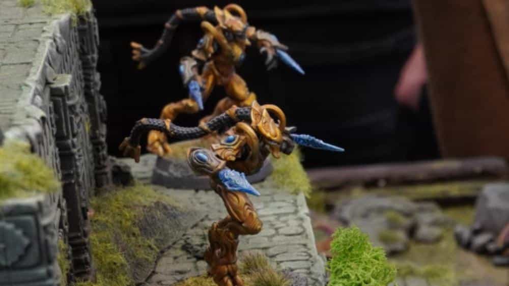 Painted Protoss-style alien warrior miniatures charging across sci-fi terrain, used as an example of StarCraft-inspired tabletop wargaming units.